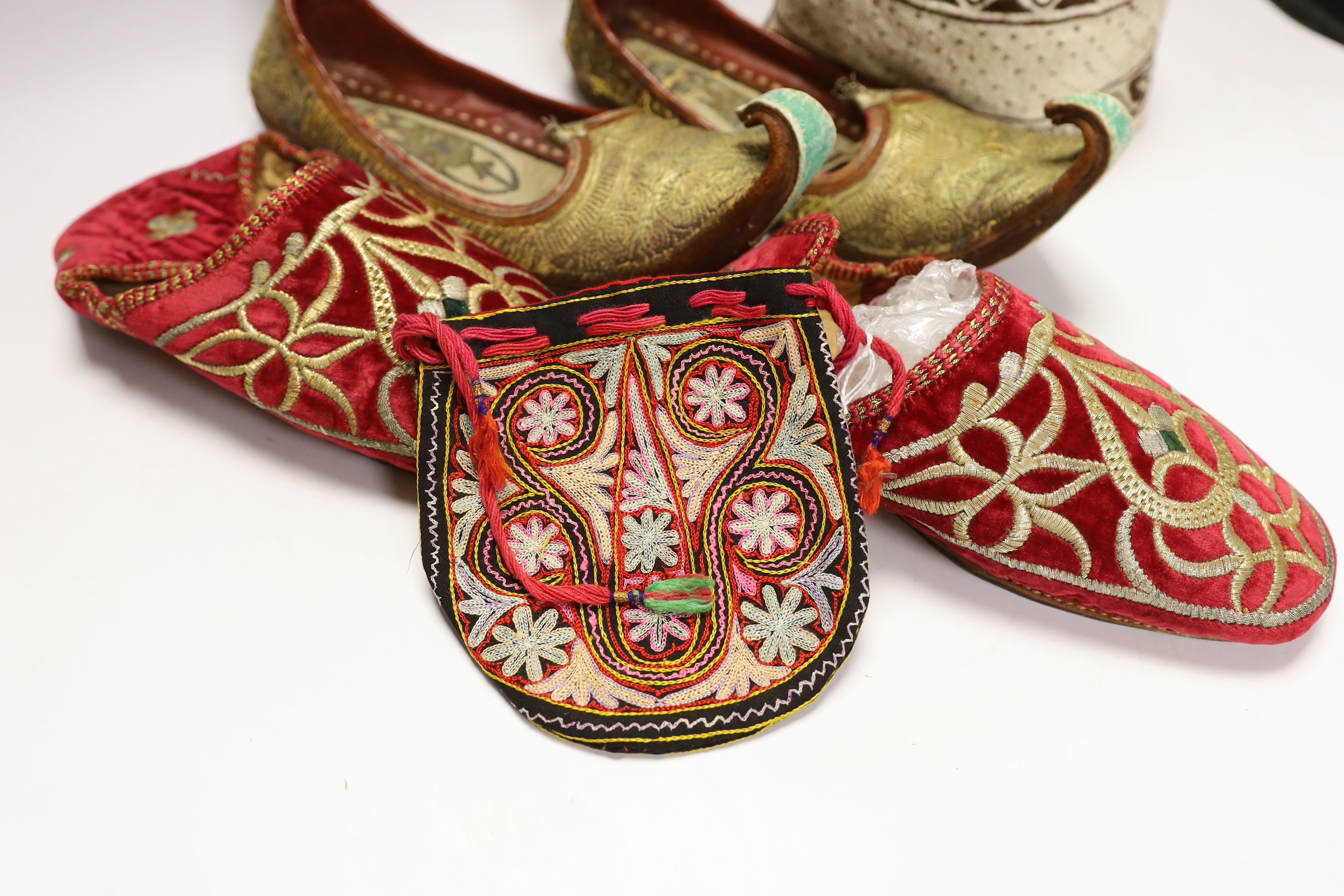A pair of early 20th century metal thread embroidered Turkish slippers, a pair of similar embroidered red velvet children’s Indian slippers, an embroidered chain stitch drawstring purse and a quilted child’s hat